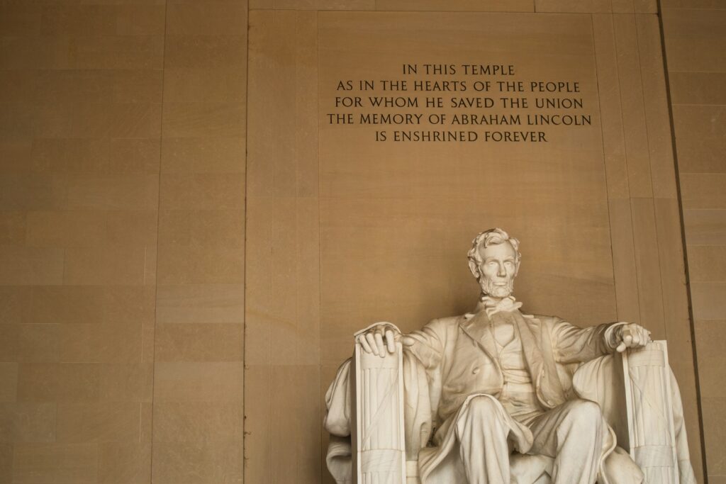 a statue of a man sitting in a chair with Lincoln Memorial in the background